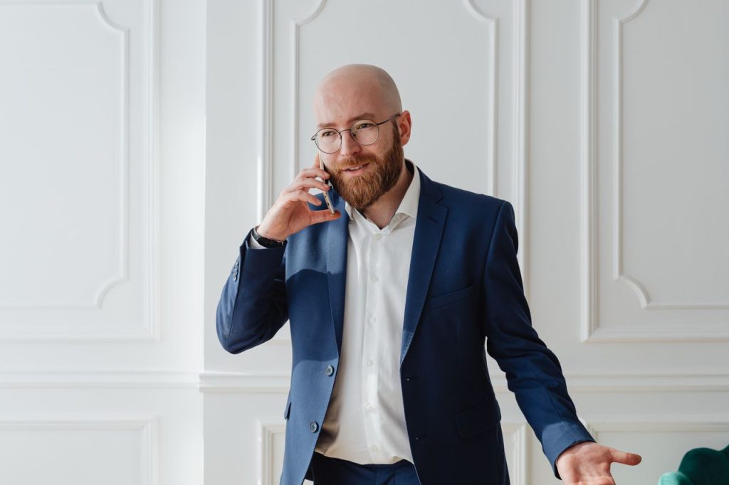Bald bearded businessman in a suit having a phone call indoors.