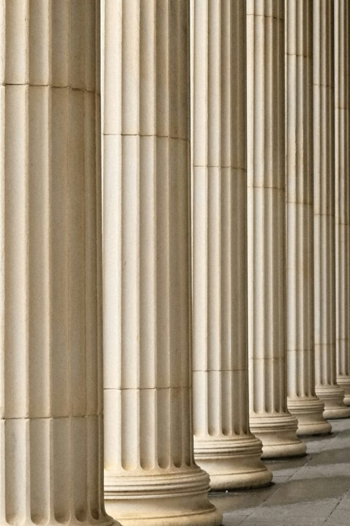 a-person-sitting-on-a-bench-in-front-of-a-row-of-pillars-6x4ldxv3x4o