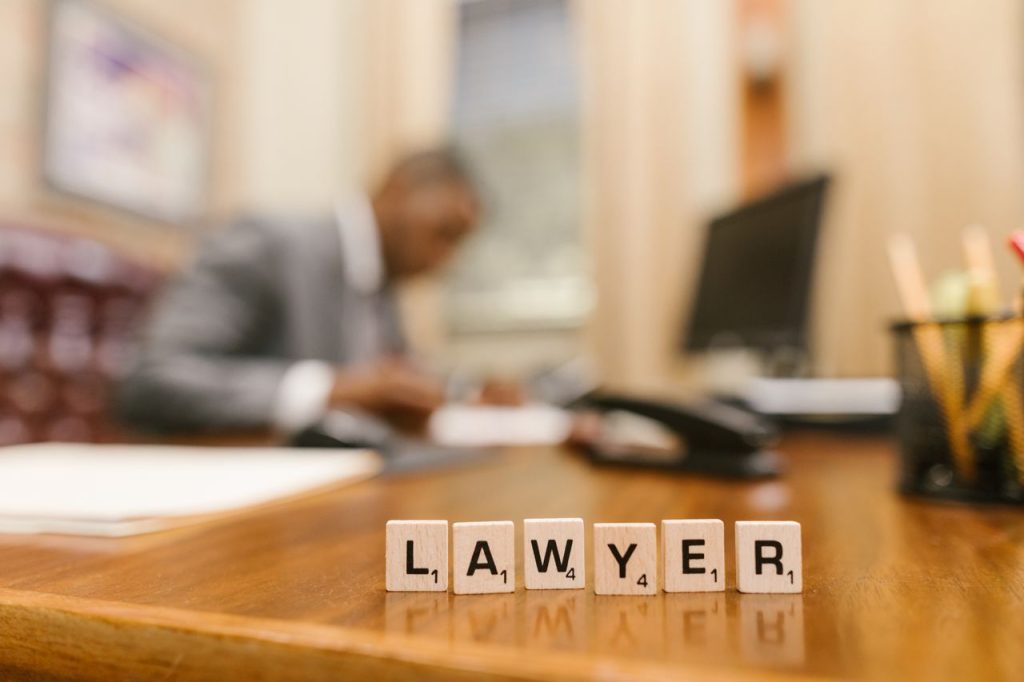 Wooden letter tiles spelling LAWYER on a desk, with blurred office setting in the background.