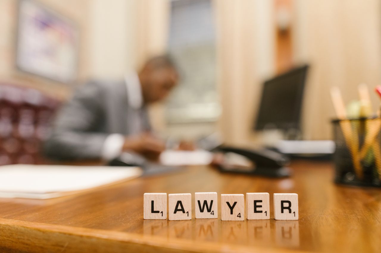 Wooden letter tiles spelling LAWYER on a desk, with blurred office setting in the background.