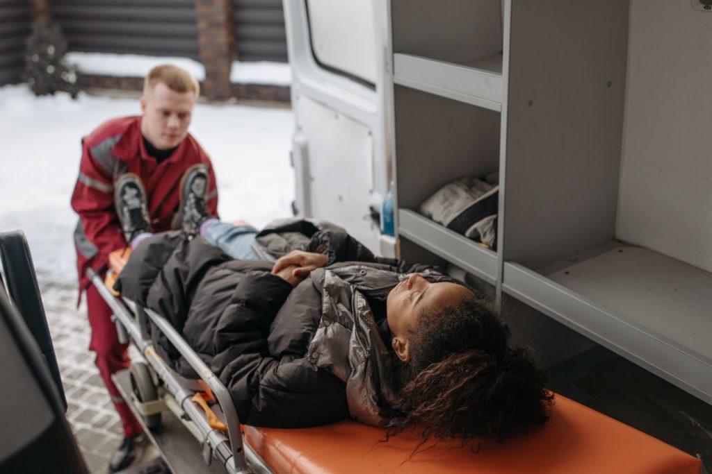 Emergency medical technicians assisting a patient onto a stretcher and into an ambulance.